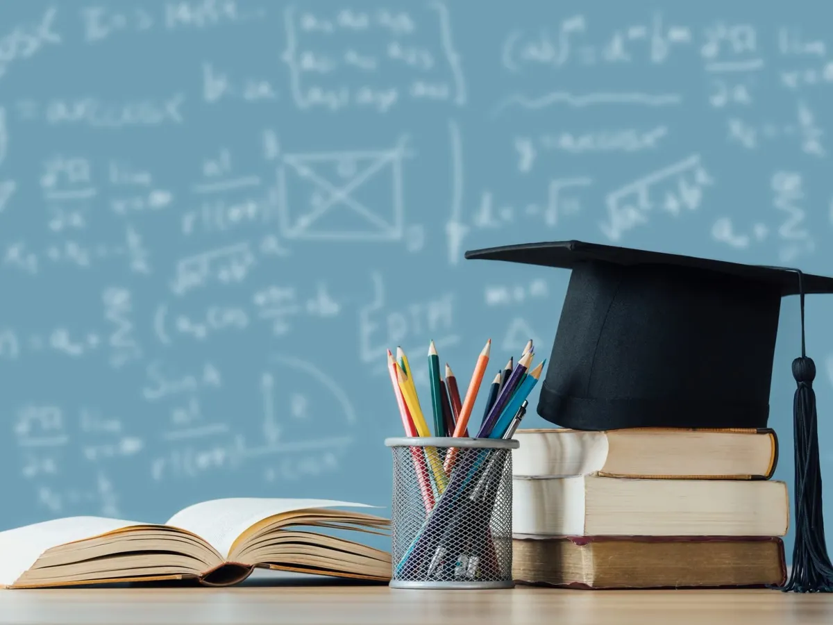 a black board with formulas, a collection of books, and a graduation cap